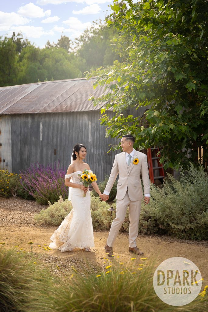 Bride and groom under sunflower arch by Daisy’s Flowers at OC outdoor ceremony by D. Park Studios
