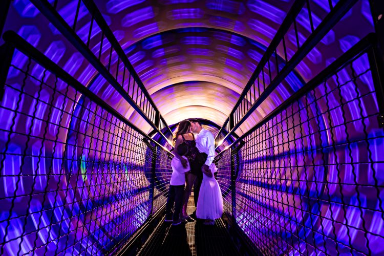 Pregnant mom, dad, big brother, new big sister give kisses and hugs to celebrate upcoming baby in maternity photoshoot at the Vortex Tunnel in the Museum of Illusions in San Diego