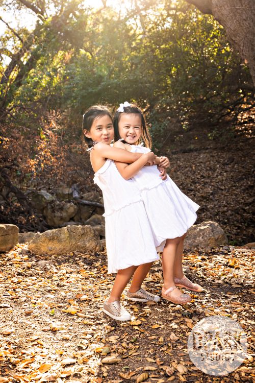 Big sister carries little sister in playful sisters family photo at Oak Canyon Nature Center in Anaheim Hills